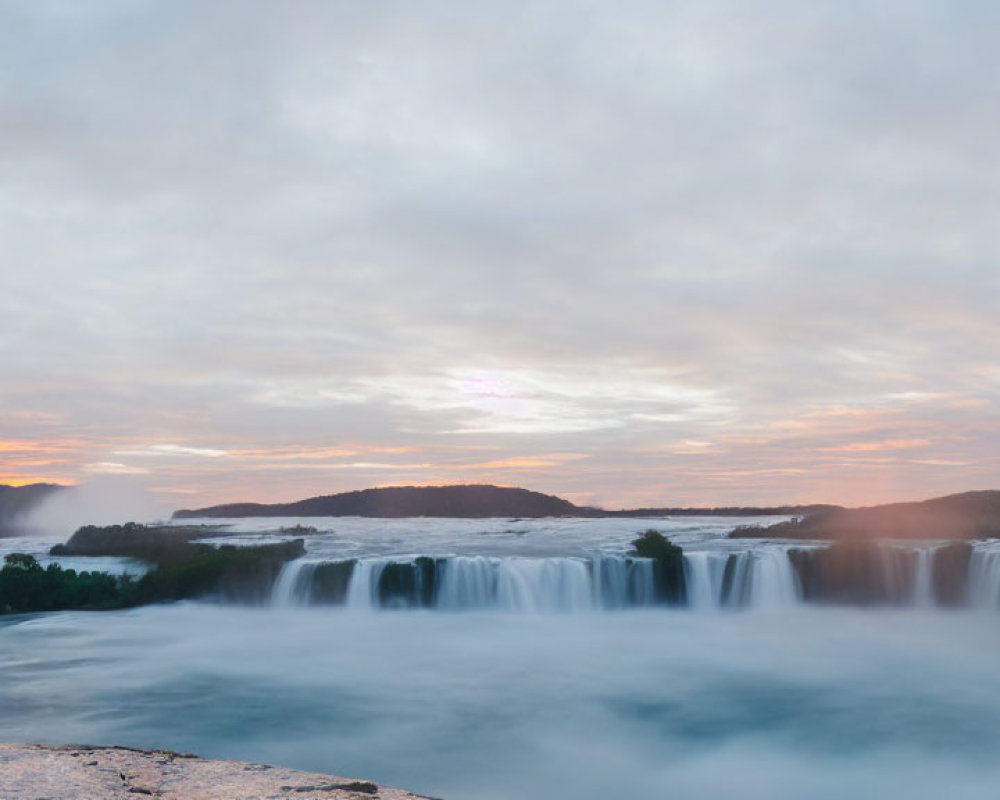 Tranquil waterfall scene with evening sky and distant hills