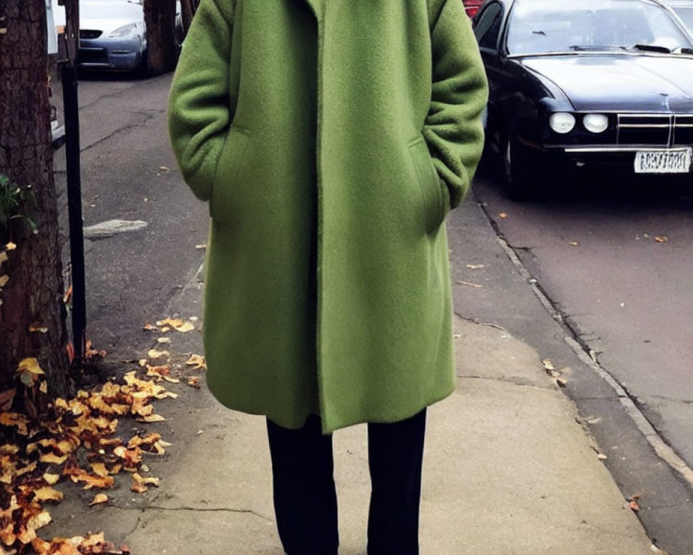 Person in Large Green Coat Standing on Sidewalk with Fallen Leaves
