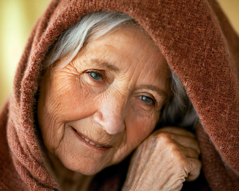 Elderly woman in brown hooded garment with gentle smile and sparkling eyes