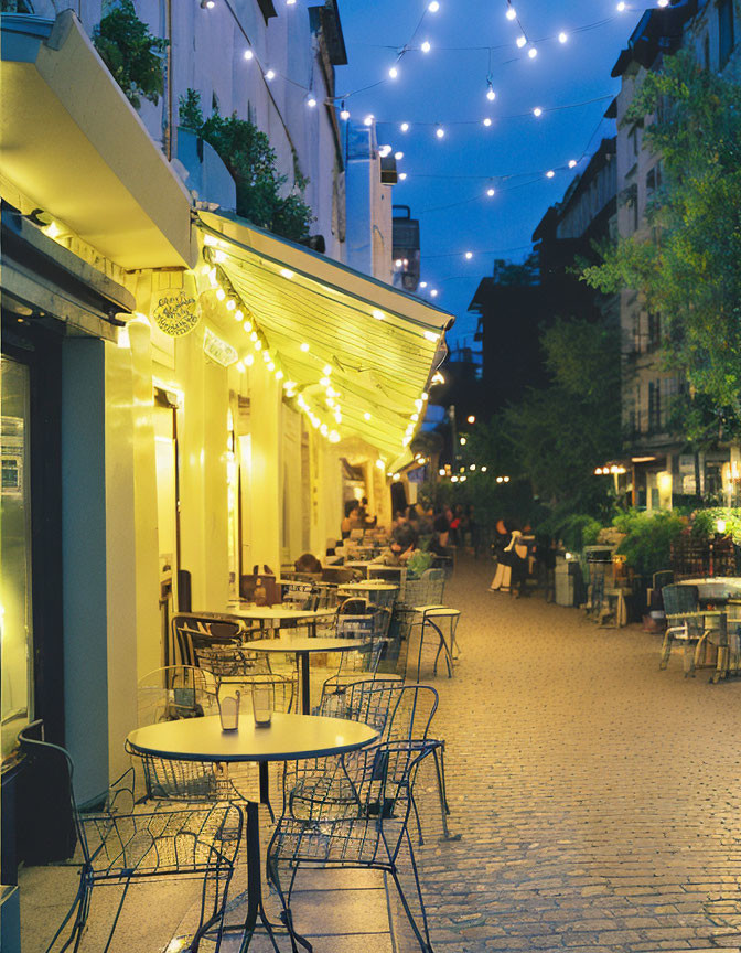 Outdoor cafe scene with string lights, empty chairs, warm shopfront glow on cobblestone street