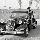 Person in Top Hat and Sunglasses with Classic Car in Skull-filled Scene