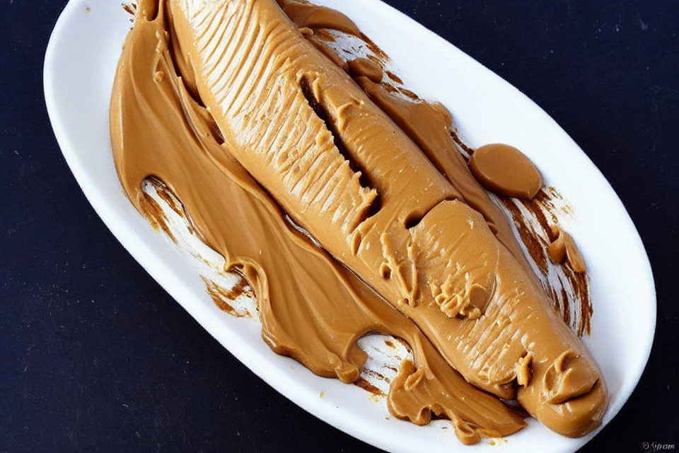 Creamy Peanut Butter Spread on Oval White Plate Against Dark Background