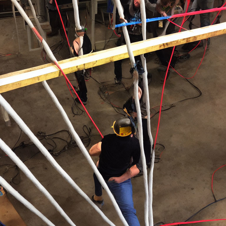 Person in Yellow Hard Hat in Workshop Setting with Others Working