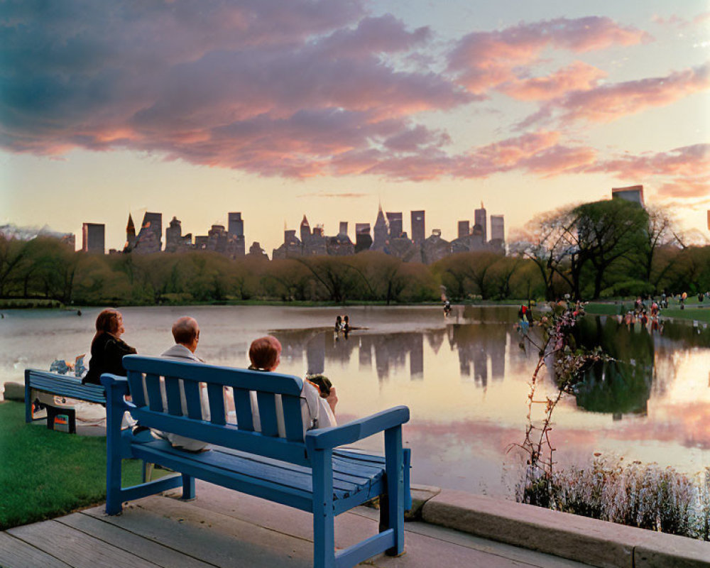People on Blue Bench by Lake in Park at Sunset Facing City Skyline