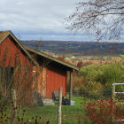 Vibrant autumn landscape with red barns, golden trees, fence, and rolling hills