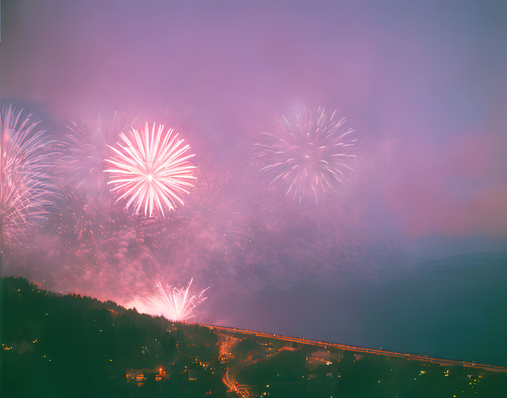 Colorful fireworks display over coastal road at dusk with ocean backdrop