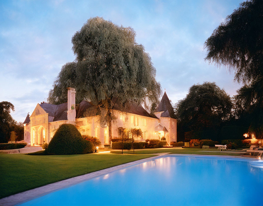 Twilight estate with illuminated interior, pool, lawn, and tree