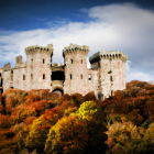 Stone castle in autumn forest under cloudy sky with red flag