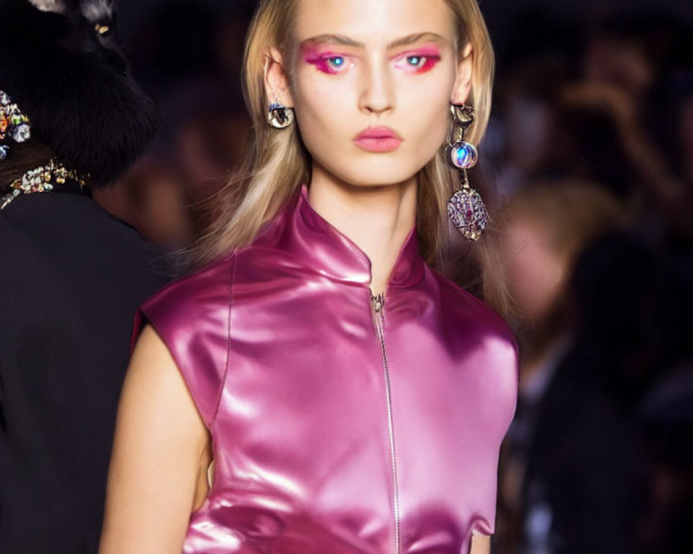 Model with bold pink eye makeup, large earrings, shiny purple top, and black cat.
