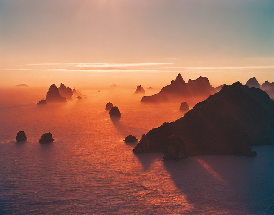 Tranquil sunset over misty sea with silhouetted rocks