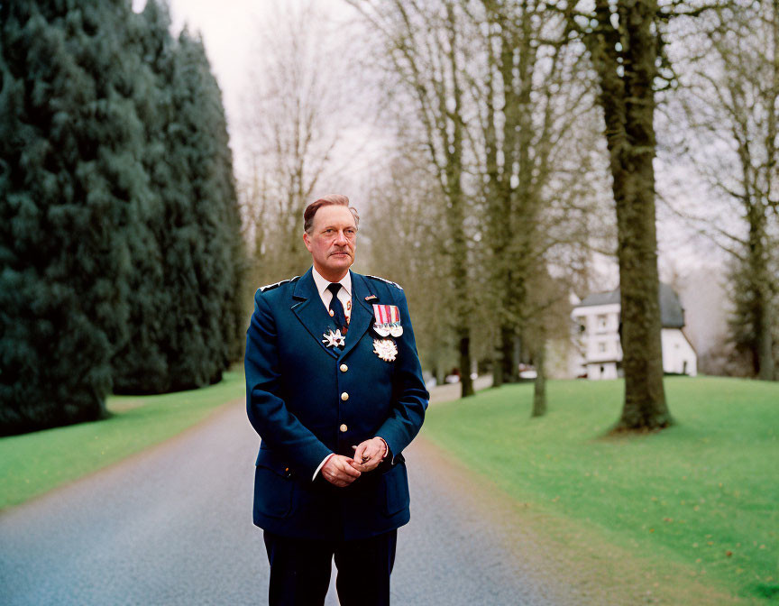 Military man in formal uniform with medals standing on tree-lined path