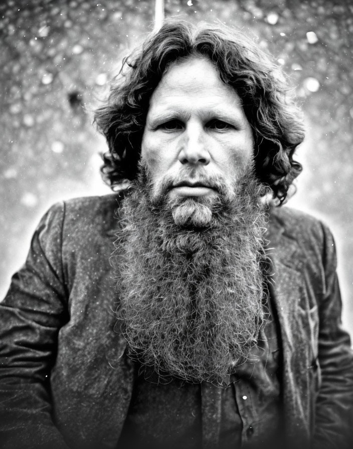 Monochrome portrait of bearded man with curly hair in snowfall
