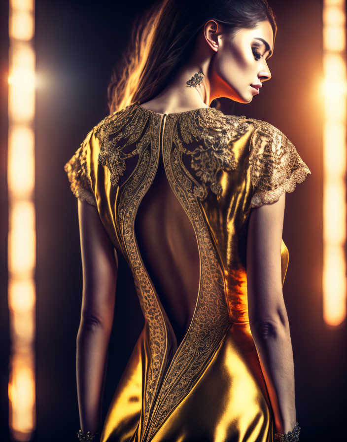 Woman models elegant gold dress with lace back design in dramatic lighting