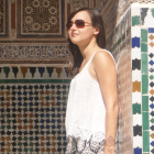 Woman in white top and floral skirt next to tiled wall.