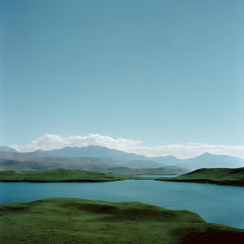 Tranquil landscape with green hills, blue lake, and mountains