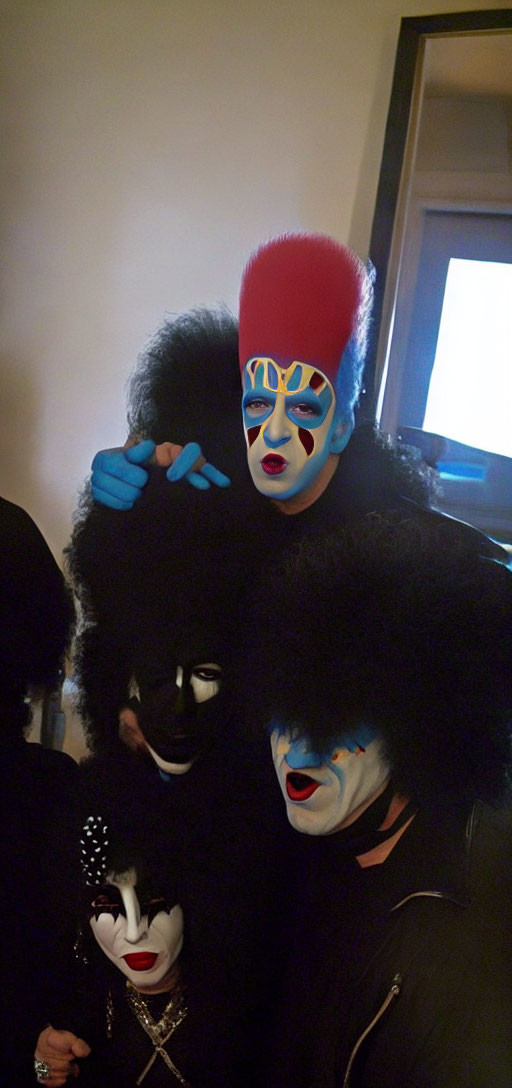 People in dark setting with face paint and wigs like rock band members.