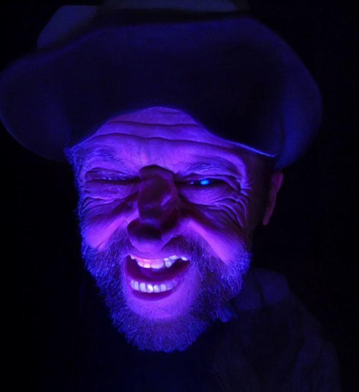 Smiling person with hat under blue light, mysterious face focus