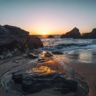 Tranquil sunset beachscape with bioluminescent waves and rocky formations