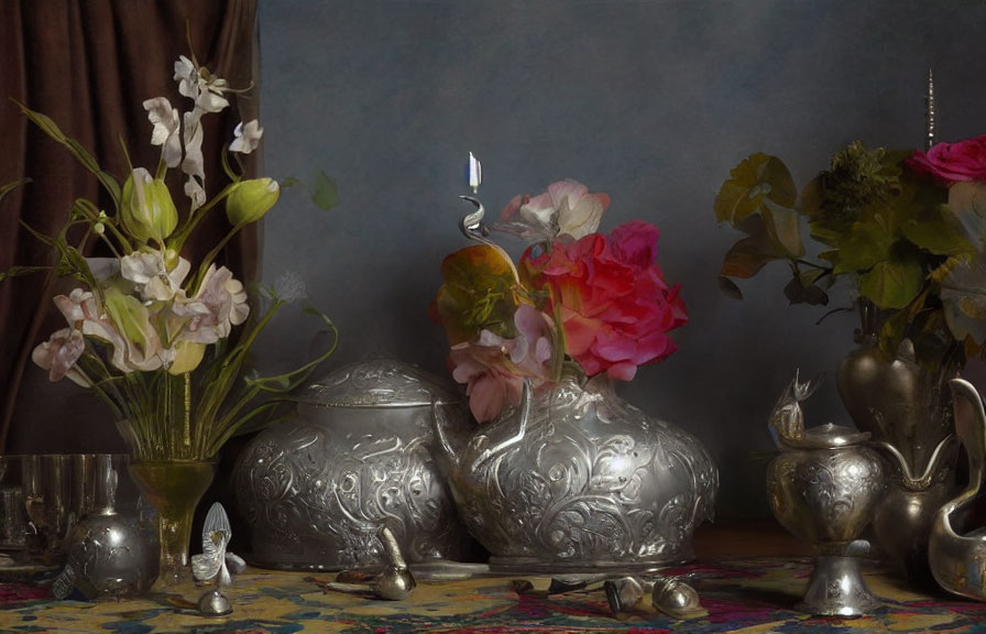 Silver teapots, candle, flowers on draped table against grey backdrop