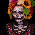 Colorful Day of the Dead skull face paint with floral crown and body decorations