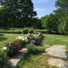Scenic garden path with flowering plants, stones, green tree, and blue sky