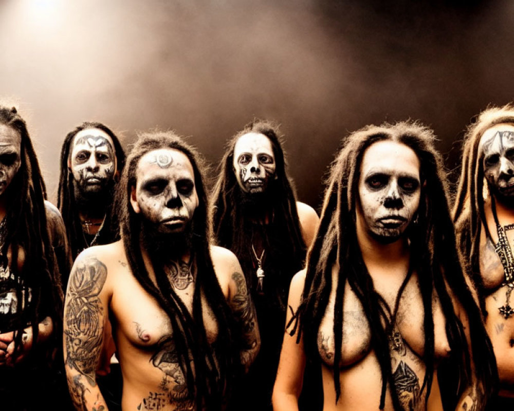 Seven individuals with dark makeup and dreadlocks in intense expressions against a smoky backdrop