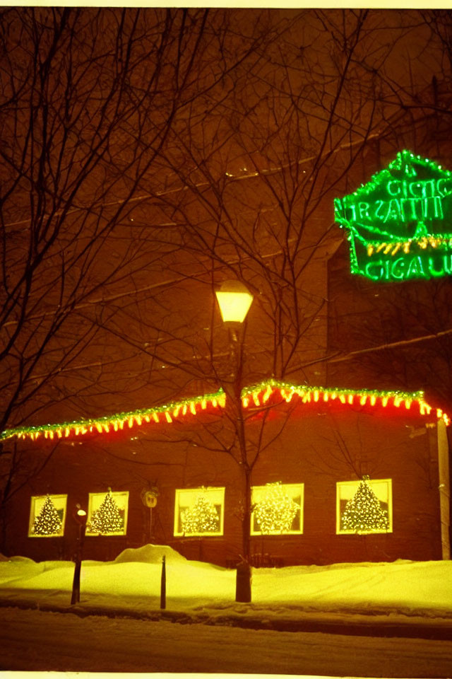 Snow-covered brick building with Christmas lights and wreaths, glowing streetlamp and neon sign.