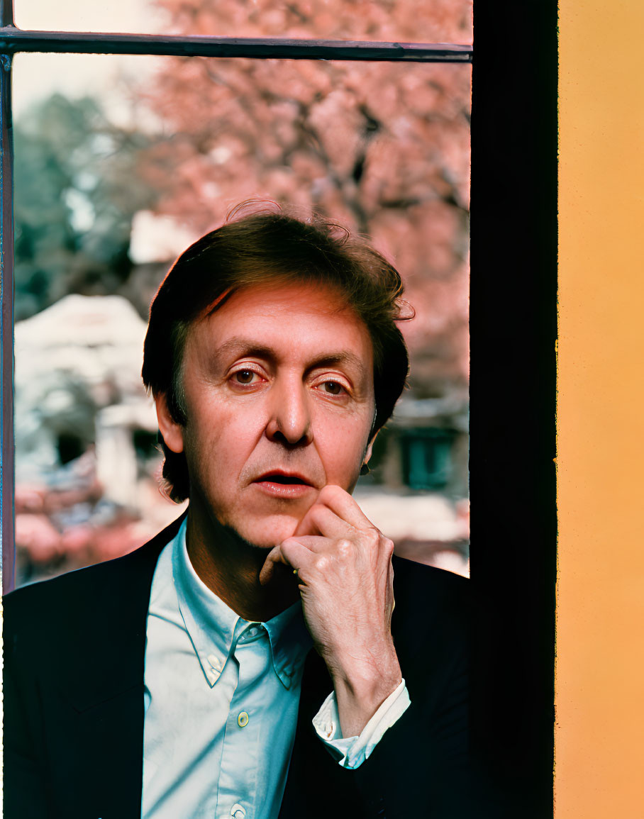 Contemplative man by window with pink blossoms, framed in vivid yellow and black.
