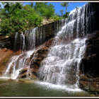 Lush greenery surrounds vibrant multi-tiered waterfall