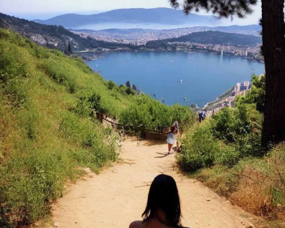 Dark-haired person gazes at scenic lake and hills under clear sky.
