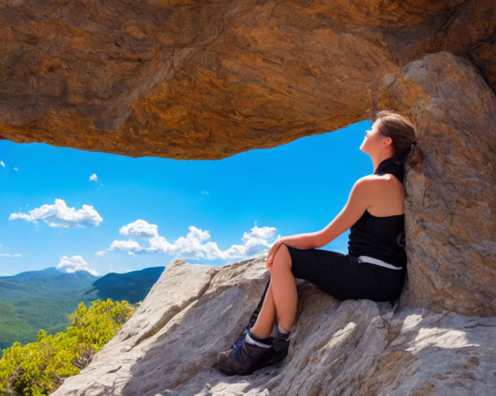 Person sitting under rock overhang admiring mountain landscape