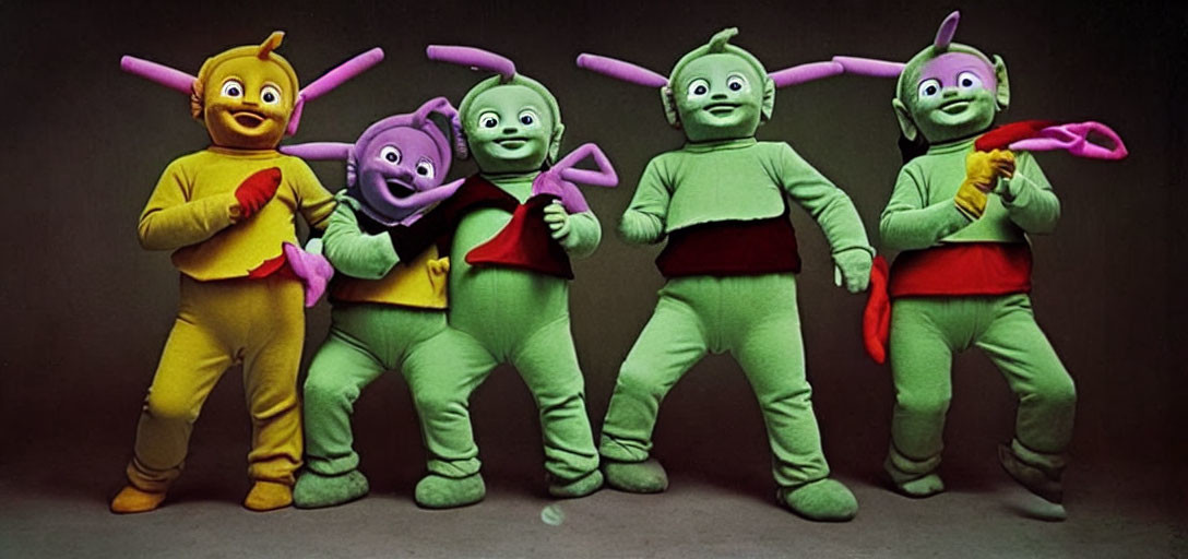 Four individuals in colorful costumes with antennae and smiling faces standing side-by-side