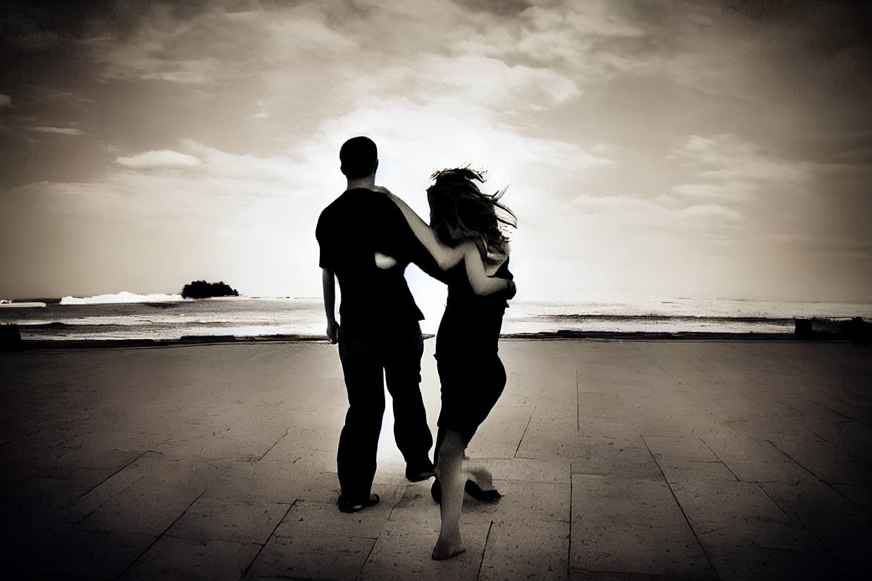 Silhouetted couple dancing by the sea under a cloudy sky
