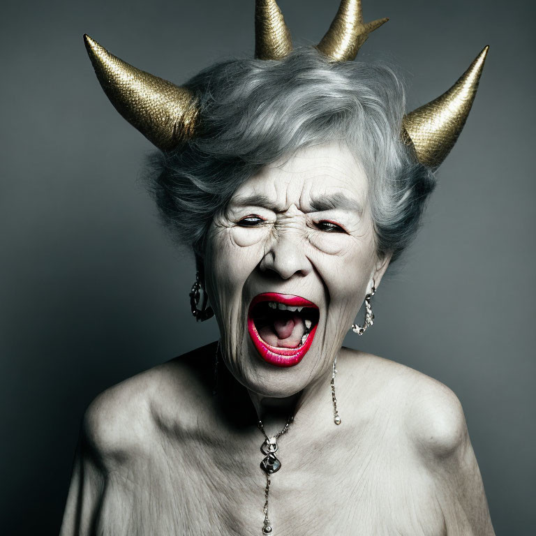 Elderly woman with spiked golden horns snarling in necklace, grey backdrop