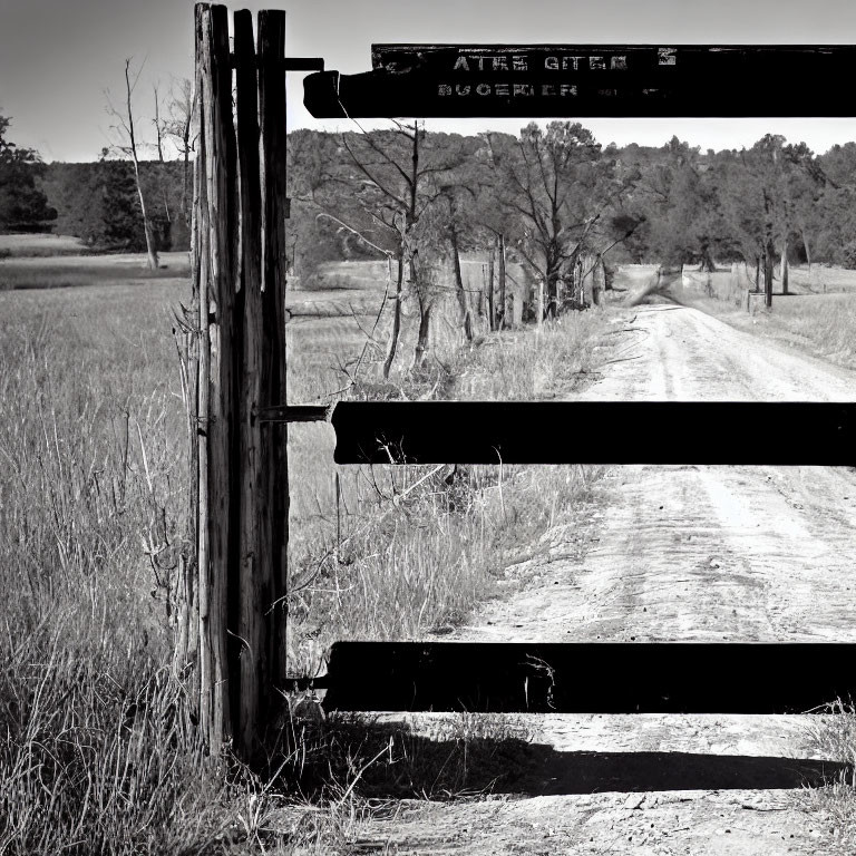 Monochrome photo of rustic wooden gate on dirt road