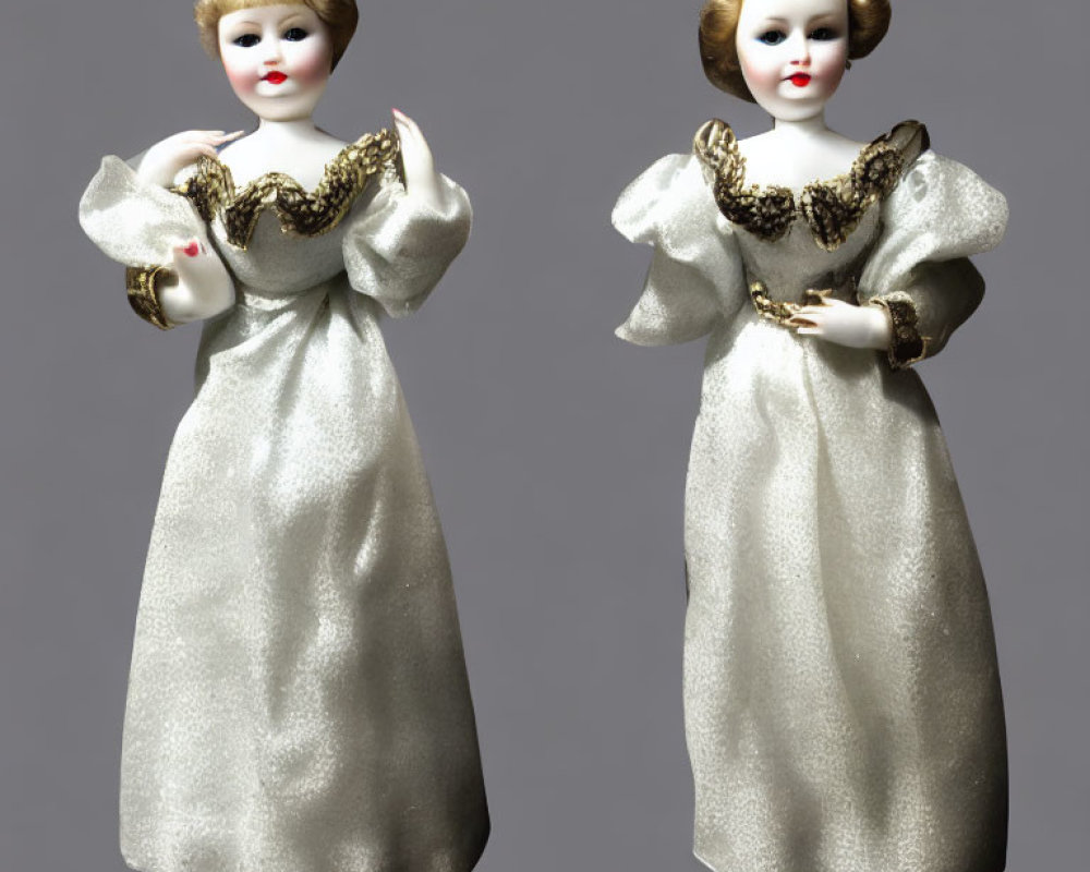 Vintage porcelain dolls with pale complexions in golden and white dresses on grey background