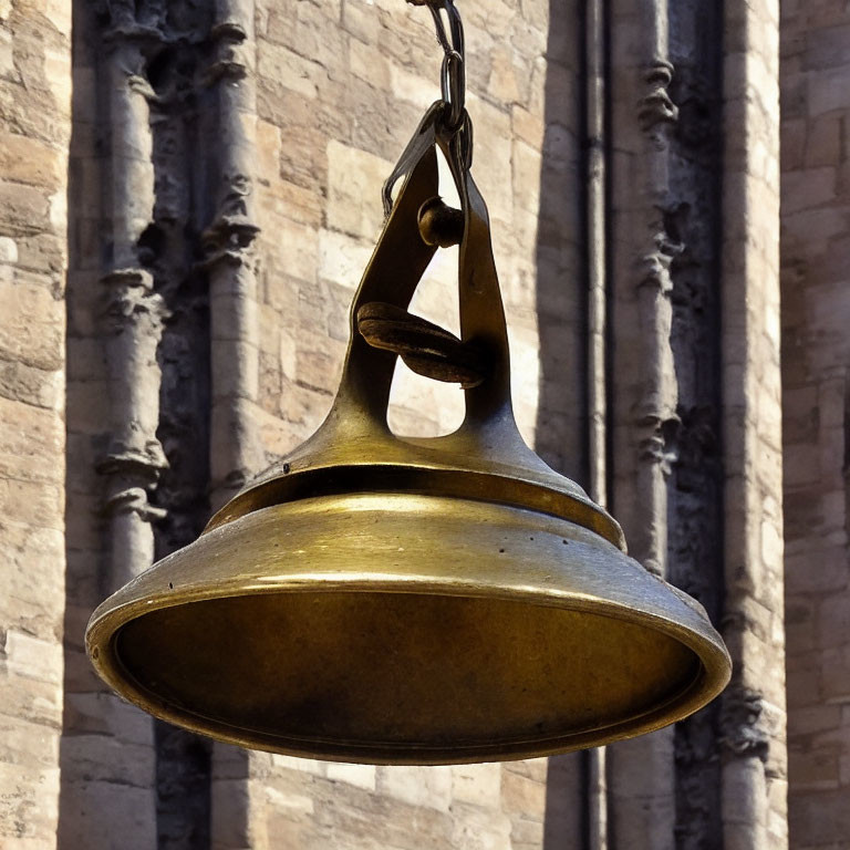 Brass bell on metal chain near stone building with sculpted details