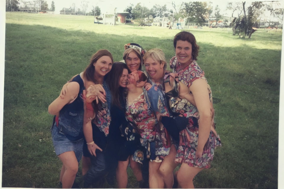 Five friends posing playfully in summer outfits on grassy field