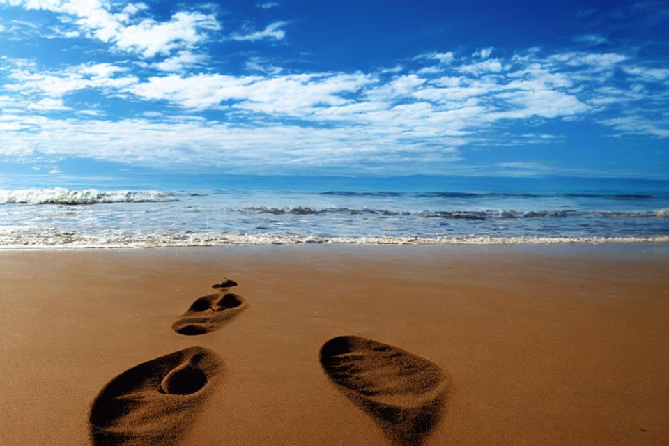 Tranquil beach scene with footprints, gentle waves, and blue sky