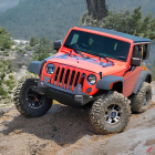 Red Jeep Wrangler off-roading in rugged sandy landscape