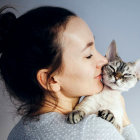 Woman with bun hairstyle holding two white cats on gray background
