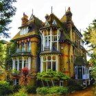 Intricate Victorian mansion with turrets and balconies, surrounded by autumn trees