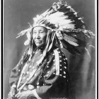 Portrait of person in Native American headdress with feathers and beads on grayscale background
