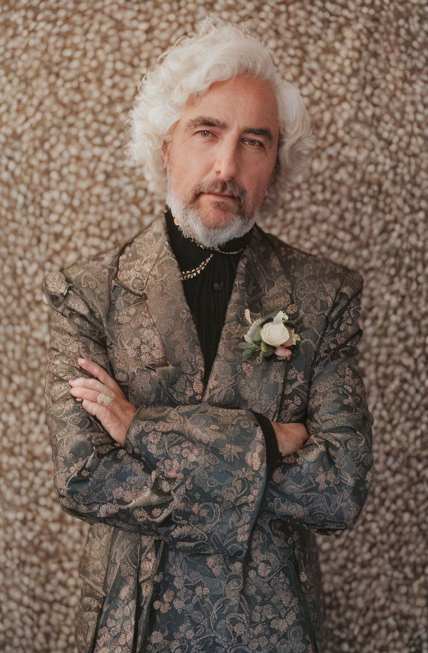 White-haired man in patterned suit with crossed arms on textured background