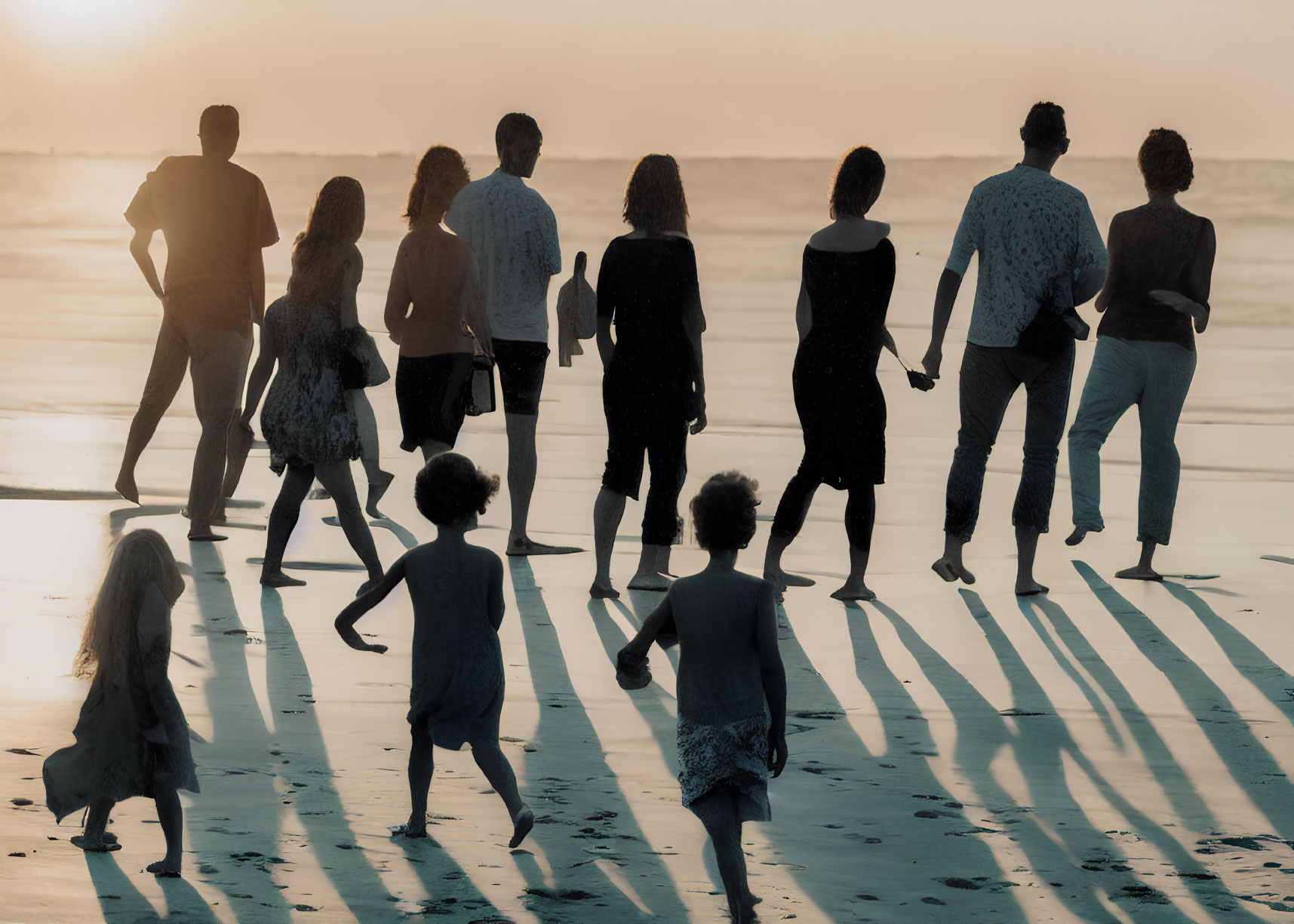 Group of people walking on beach at sunset with long shadows