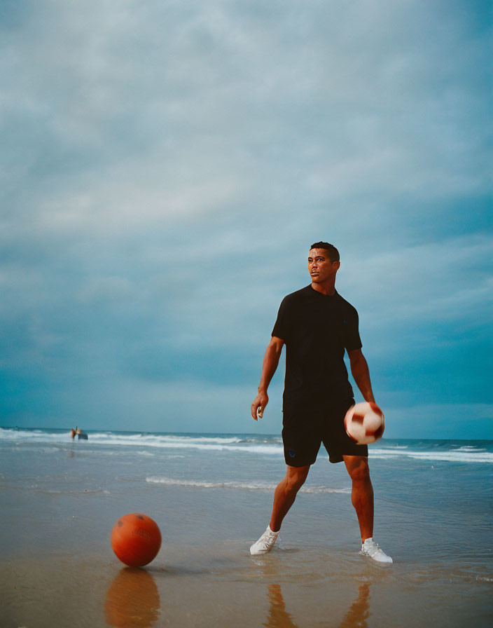 Man in black outfit playing football on beach under overcast sky