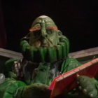 Humanoid alien with tentacles reading a book beside a bespectacled man in green formal attire