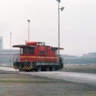 Red Diesel Locomotive Passing Industrial Factories Under Hazy Sky