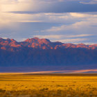 Tranquil sunset landscape: golden hills, rugged mountains, soft blue sky