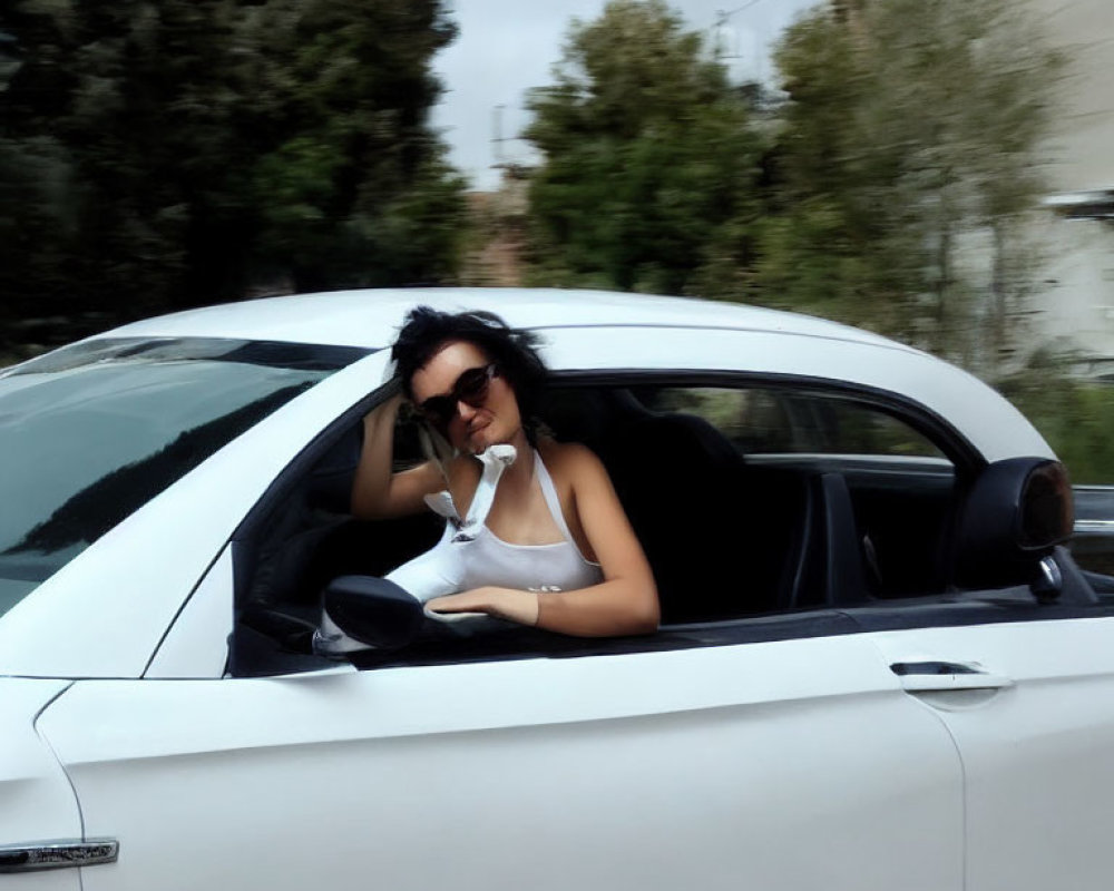 Person in sunglasses and white top leans out car window with relaxed posture.